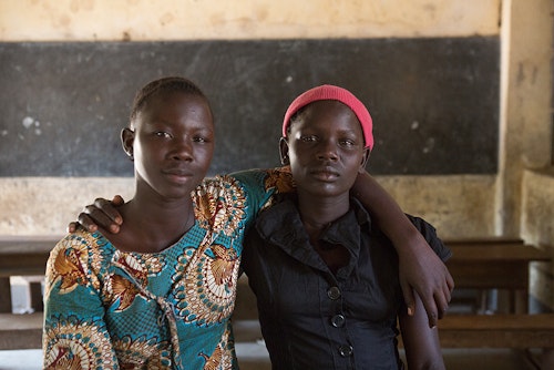 فتاتان أوغنديتان تحملان يد بعضهما البعض وتبتسمان للكاميرا داخل الفصل الدراسي