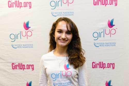 Alex Leone_2013-2014 Teen Advisor (close angle headshot, a picture little blurry ) a teen girl wearing her girl up white shirt with her smiley face facing the camera, and background is girlup.org board