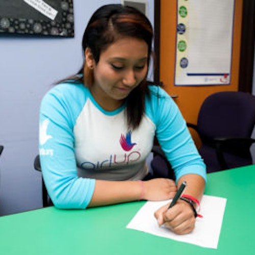 Angie Partida_The founding class of Teen Advisors(straight angle, but not a clear picture ) a teen girl wearing her girl up blue long shirt with her smile face facing down and holding a pen on her notebook, and background is an office