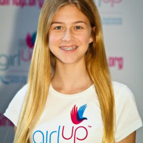 Annie Gersh_Grupo de Consejeras adolescentes 2011-2012 (retrato en primer plano, fotografía un poco borrosa); una adolescente con la camiseta blanca de Girl Up, sonriendo a la cámara, con el cartel de girlup.org de fondo.