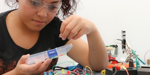 uma menina usando óculos de laboratório e testando electricidade em uma mesa