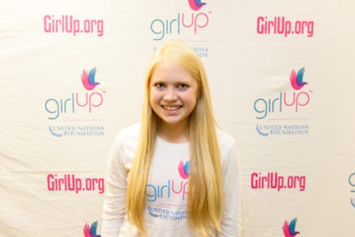 Carly Bandt_2013-2014 Teen Advisor (close angle headshot, a picture little blurry ) a teen girl wearing her girl up white shirt with her smiley face facing the camera, and background is girlup.org board