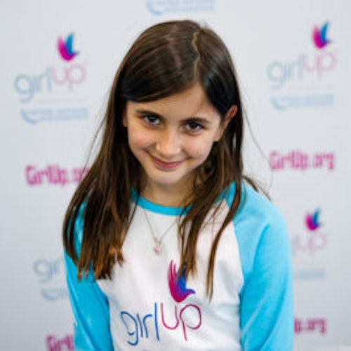 Darya Pishevar_首届青年顾问（近距离头像照，画面不清晰），照片中的她穿着蓝色 Girl Up 长袖 T 恤，头微低看着镜头微笑，照片背景为 girlup.org 活动展板