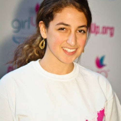 Eliora Katz_家乡： 美国华盛顿特区_2011-2012 届（即第二届）青年顾问（近距离头像照），照片中的她穿着白色 Girl Up T 恤，面对镜头微笑，照片背景为 girlup.org 活动展板