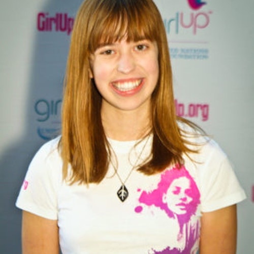 Emily Harwell_Grupo de Consejeras adolescentes 2011-2012 (retrato en primer plano); una adolescente con la camiseta blanca de Girl Up, sonriendo a la cámara, con el cartel de girlup.org de fondo.