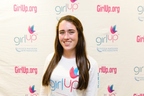 Emma Knoll_2013-2014 Teen Advisor (close angle headshot, a picture little blurry ) a teen girl wearing her girl up white shirt with her smiley face facing the camera, and background is girlup.org board