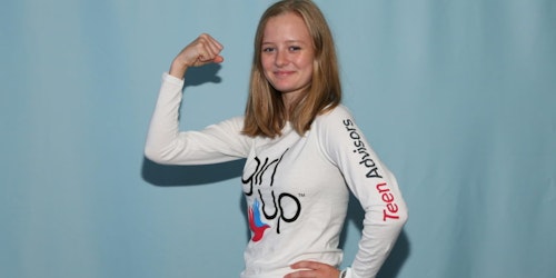 Eva, Consejera adolescente (con la camiseta de Girl Up), en pose de Mujer Maravilla para la cumbre (con fondo azul).