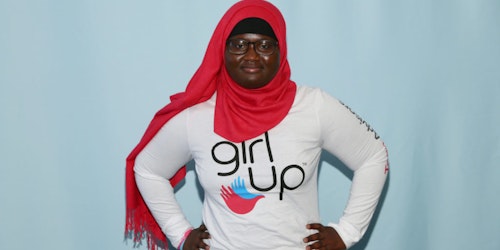 A consultora adolescente Fatimata, com a camiseta da Girl Up, faz pose de supermulher para a foto do evento (plano de fundo azul)