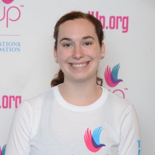 Hayley Peacock_Consejera adolescente 2014-2015 (retrato en primer plano); una adolescente con la camiseta blanca de Girl Up, sonriendo a la cámara, con el cartel de girlup.org de fondo.