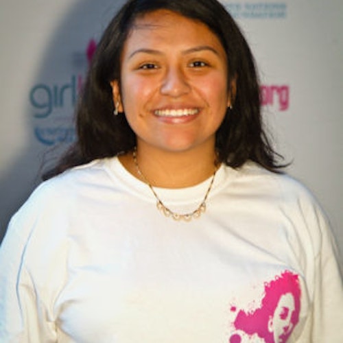Itzel Delgado，联合主席_家乡： 美国纽约州纽约市_2011-2012 届（即第二届）青年顾问（近距离头像照），照片中的她穿着白色 Girl Up T 恤，面对镜头微笑，照片背景为 girlup.org 活动展板