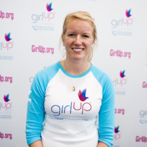 Jenna Bailey_首届青年顾问（近距离头像照，画面不清晰），照片中的她穿着蓝色 Girl Up 长袖 T 恤，面对镜头微笑，照片背景为 girlup.org 活动展板