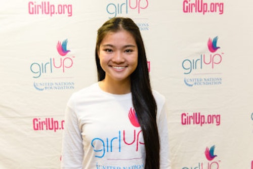 Kaitlin Hung_2013-2014 Teen Advisor (close angle headshot, a picture little blurry ) a teen girl wearing her girl up white shirt with her smiley face facing the camera, and background is girlup.org board