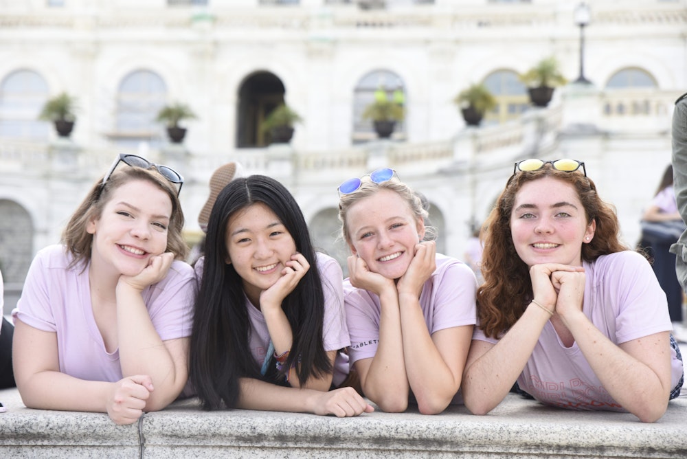 4 Girl Up girls with a different ethnic group holding their head and laying in front of the capitol in DC