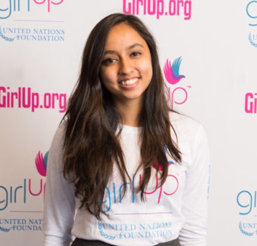Lavanya Singh, Co-Chair 2017-2018 Teen Advisors, (headshot) wearing her girl up white shirt with her smiley face facing the camera, and background is girlup.org board