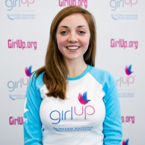 Lily Kaplan_首届青年顾问（近距离头像照，画面不清晰），照片中的她穿着蓝色 Girl Up 长袖 T 恤，面对镜头微笑，照片背景为 girlup.org 活动展板