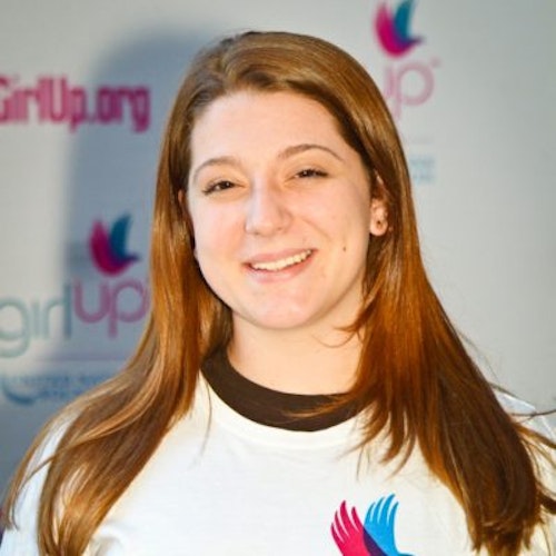 Lucy Lohrmann_家乡： 美国新泽西州哈斯布鲁克海茨_2011-2012 届（即第二届）青年顾问（近距离头像照），照片中的她穿着白色 Girl Up T 恤，面对镜头微笑，照片背景为 girlup.org 活动展板