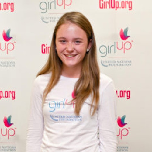Meghan Murray, Hometown: Chevy Chase, MD_2012-2013 Class Teen Advisors (close angle headshot, a little blurry picture ) a teen girl wearing her girl up white shirt with her smiley face facing the camera, and background is girlup.org board