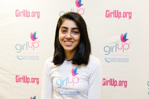 Mehar Gujral_2013-2014 Teen Advisor (close angle headshot, a picture little blurry ) a teen girl wearing her girl up white shirt with her smiley face facing the camera, and background is girlup.org board