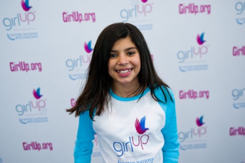 Mia Gutierrez, The founding class of Teen Advisors(close angle, but not clear picture headshot ) a teen girl wearing her girl up blue long shirt with her smiley face facing the camera, and background is girlup.org board