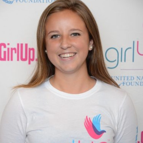 Morgan Wood_Consejera adolescente 2014-2015 (retrato en primer plano); una adolescente con la camiseta blanca de Girl Up, sonriendo a la cámara, con el cartel de girlup.org de fondo.