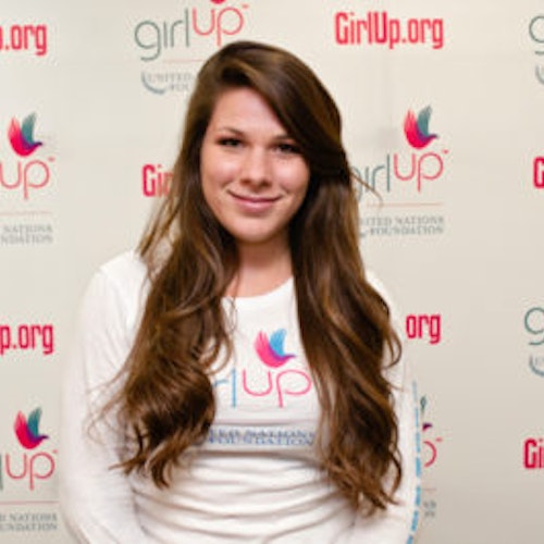 Natasha Madorsky_家乡： 美国俄亥俄州克里夫兰_2012-2013 届青年顾问（近距离头像照，画面有点模糊），照片中的她穿着白色 Girl Up T 恤，面对镜头微笑，照片背景为 girlup.org 活动展板