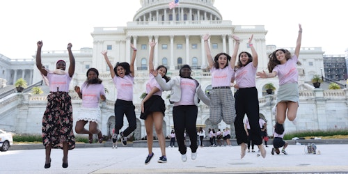 toma de ángulo completo de un grupo de chicas de Girl Up con un grupo étnico diferente hacen una foto de salto frente al capitolio en DC