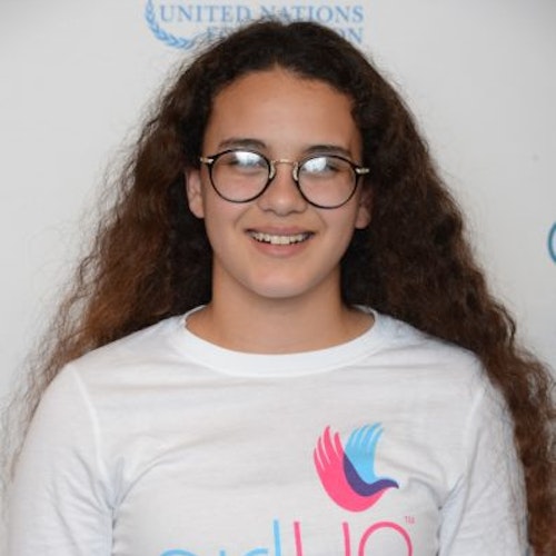 Rebecca Ruvalcaba_Jeunes conseillères 2014-2015 (portrait, angle rapproché) une adolescente portant son maillot blanc Girl Up souriant face à la caméra et en arrière plan un tableau avec l’inscription « girlup.org »