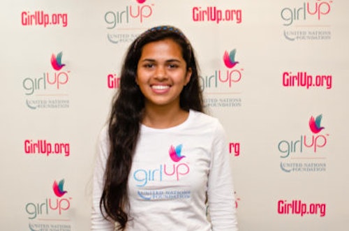 Riya Singh_2012-2013 Class Teen Advisors (close angle headshot, a picture little blurry ) a teen girl wearing her girl up white shirt with her smiley face facing the camera, and background is girlup.org board