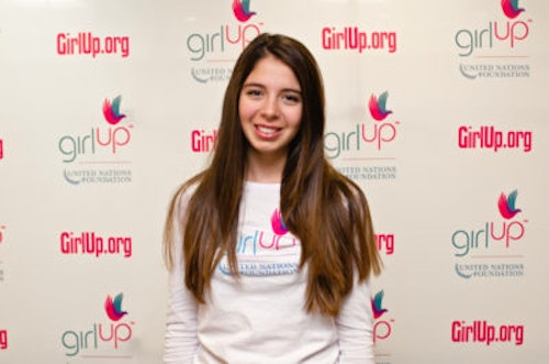 Sarah Gale Co-Chair 2013-2014 Teen Advisor (close angle headshot, a picture little blurry ) a teen girl wearing her girl up white shirt with her smiley face facing the camera, and background is girlup.org board