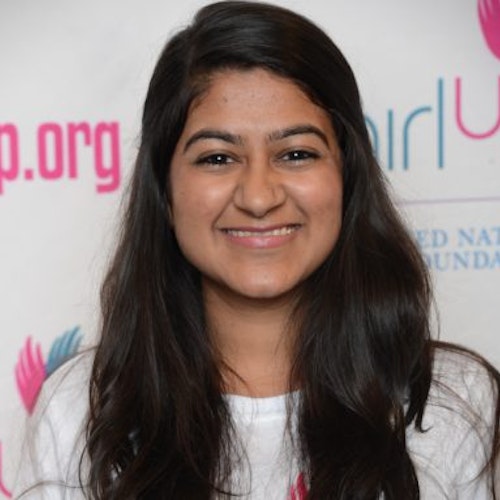 Sarah Khimjee_Consejera adolescente 2014-2015 (retrato en primer plano); una adolescente con la camiseta blanca de Girl Up, sonriendo a la cámara, con el cartel de girlup.org de fondo.