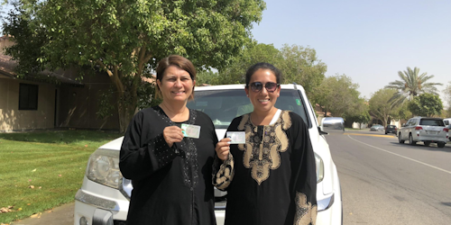 two Saudi women are holding their driver license in front of the car with big smiles