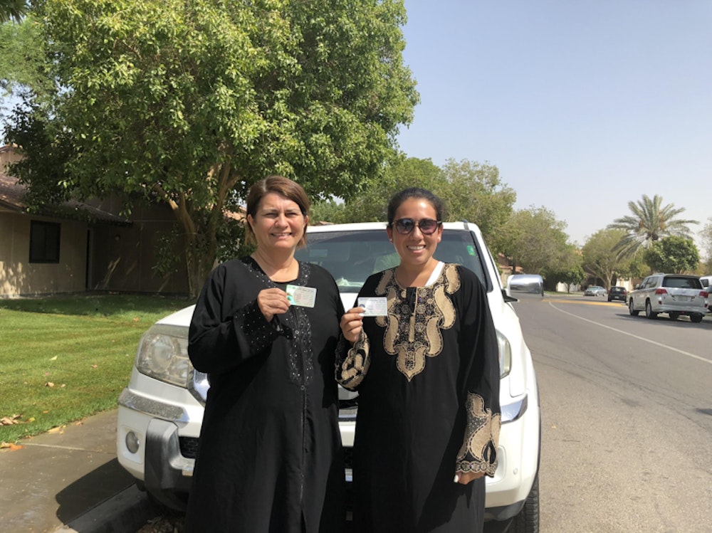 two Saudi women are holding their driver license in front of the car with big smiles