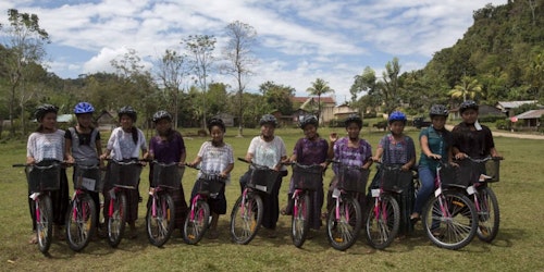 Un grupo de chicas sonriendo mientras andan en bicicleta con casco.