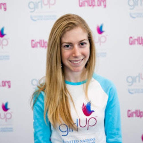 Shannon McNamara_首届青年顾问（近距离头像照，画面不清晰），照片中的她穿着蓝色 Girl Up 长袖 T 恤，面对镜头微笑，照片背景为 girlup.org 活动展板