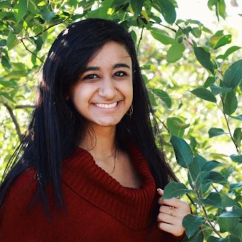 Sarina Divan, consultora adolescente de 2016-2017 (foto de perto). Uma selfie sorridente olhando para a câmera e tendo o verde das plantas como plano de fundo