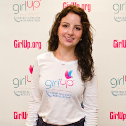 Sofia Stafford_家乡： 美国纽约州纽约市_2012-2013 届青年顾问（近距离头像照，画面有点模糊），照片中的她穿着白色 Girl Up T 恤，面对镜头微笑，照片背景为 girlup.org 活动展板