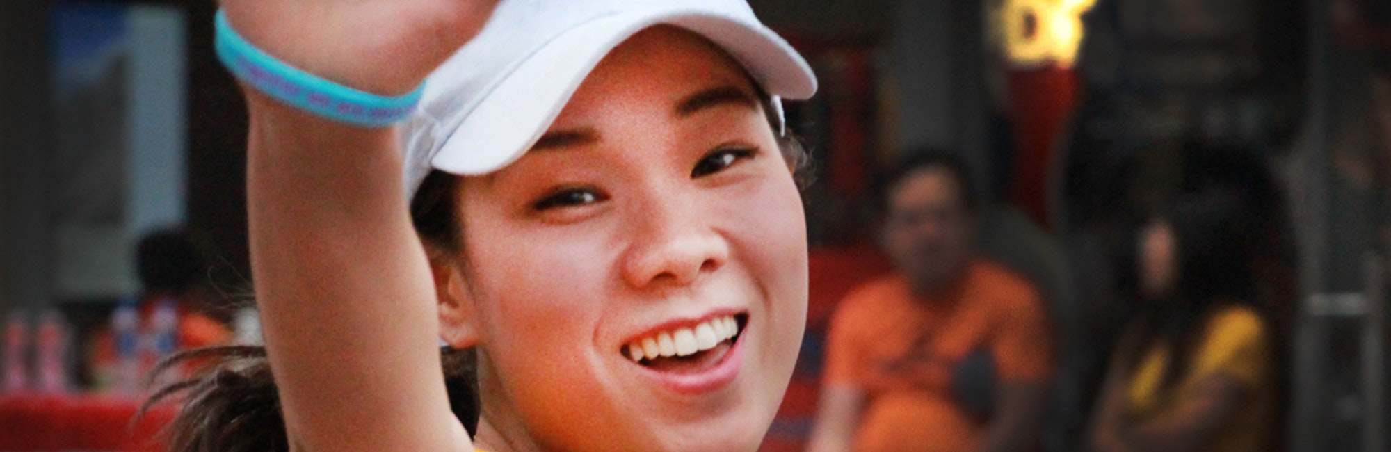 Foto em close, cortada, de uma menina sorridente, usando um uniforme de tênis