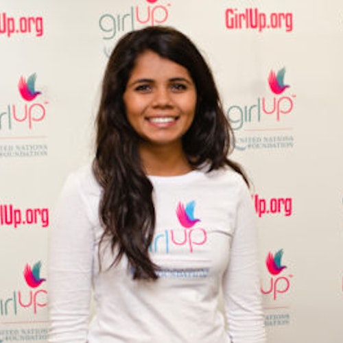 Sri Muppidi_家乡： 美国加利福尼亚州普莱森顿_2012-2013 届青年顾问（近距离头像照，画面有点模糊），照片中的她穿着白色 Girl Up T 恤，面对镜头微笑，照片背景为 girlup.org 活动展板
