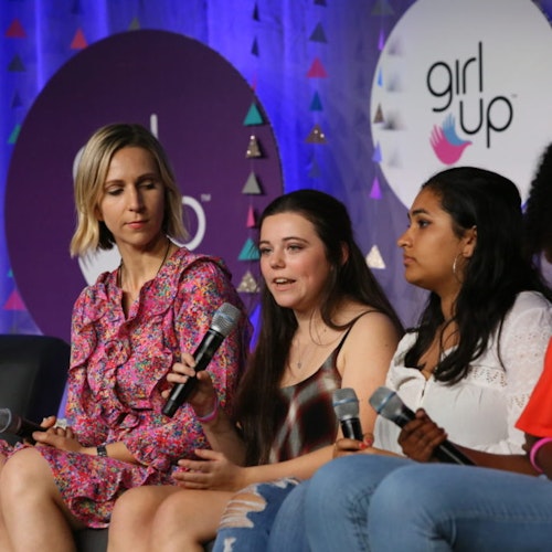 3 girls are sitting down on the couch on the stage and speaking with their mic on their hand