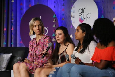 3 girls are sitting down on the couch on the stage and speaking with their mic on their hand