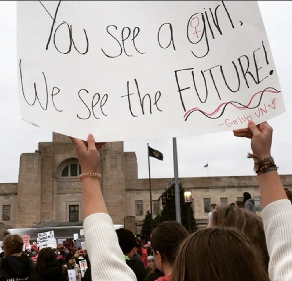 women march a girl holding a sign: "You see a girl, we see the future."