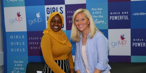 Munira Alimire taking picture with a speaker in front of the girl up borad