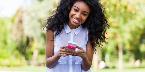 Menina sorridente olhando para a frente e segurando um telefone celular