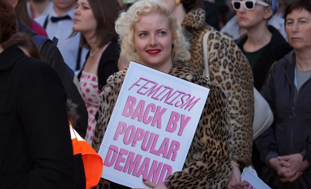 a woman holding a sign "Feminism back by popular demand"