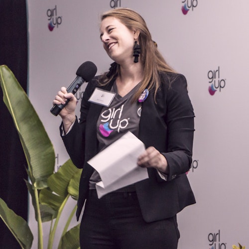 项目和影响力总监 Bailey Leuschen 穿着 Girl Up T 恤，面带笑容，手拿麦克风站在台上