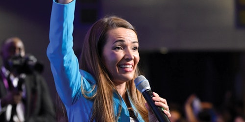 Julie Carrier is speaking with a mic on her left and she is rising her right hand up