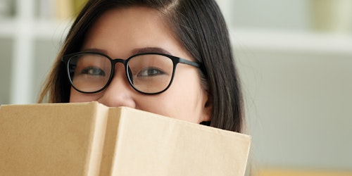a girl with a book cover her lower face with her glasses on