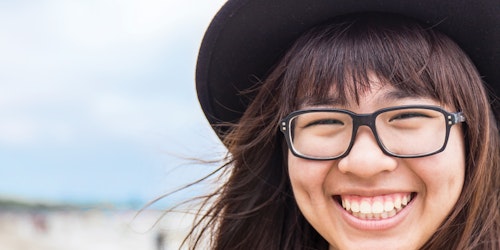 Foto em close muito perto de uma menina sorridente, usando chapéu e óculos