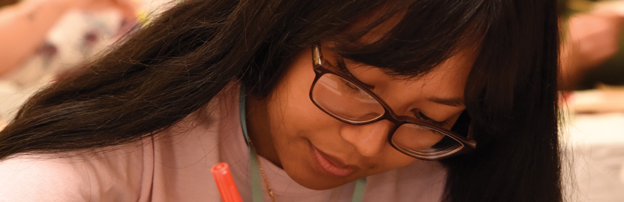 （被裁切的近距离照片）一名亚洲女孩戴着眼镜向下看，手里握着一支笔