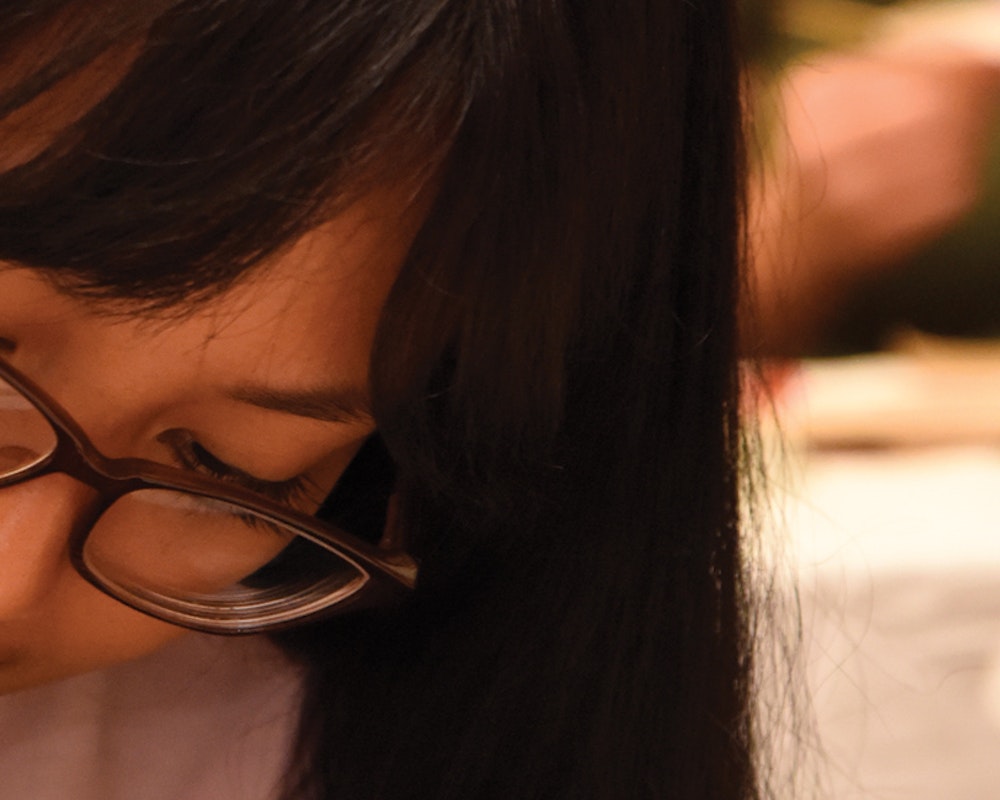 Primer plano de una chica asiática con lentes mirando hacia abajo y sosteniendo una sartén.